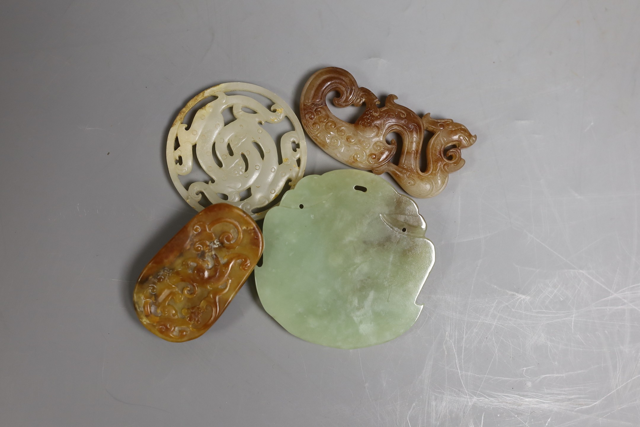 Four Chinese jade carvings, to include a face plaque, a dragon plaque, disc and a pebble carving, largest 6.5cm long, (4)